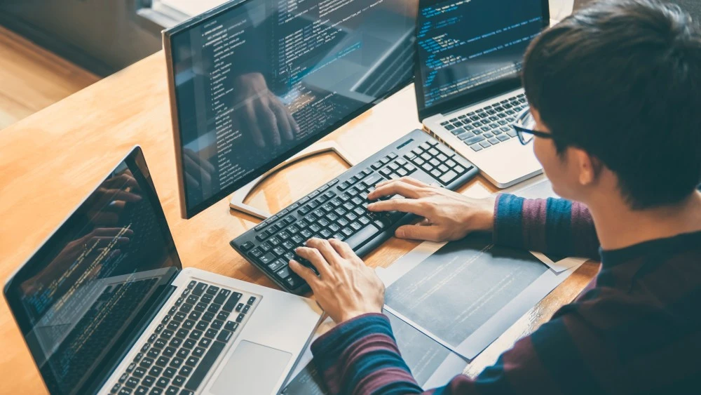 Computer Science student coding on multiple screens